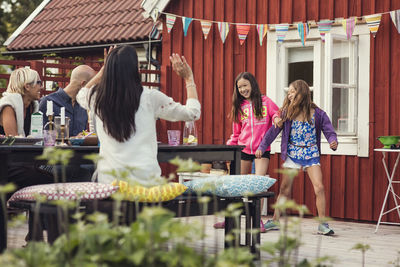 Happy family and friends watching girls dancing in back yard during garden party