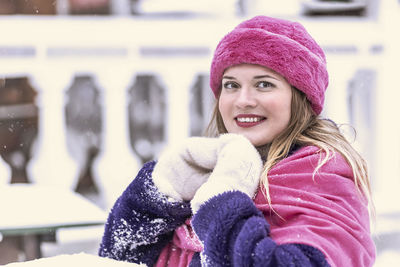 A  woman in a pink scarf and hat, white mittens and a purple fur coat outdoors in a park in winter