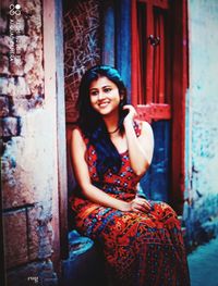 Portrait of smiling young woman standing against wall