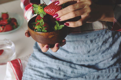 Midsection of woman holding strawberries in bowl at home