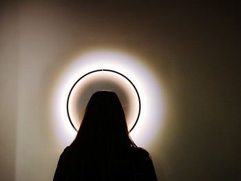 Rear view of silhouette woman standing against illuminated wall