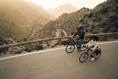 High angle view of male and female explorers cycling on road by mountains