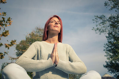 Low angle view of woman meditating while sitting against sky