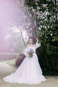 Woman holding flower bouquet against trees and plants