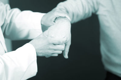 Midsection of doctor examining hand against black background