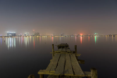 Illuminated pier over sea against sky at night