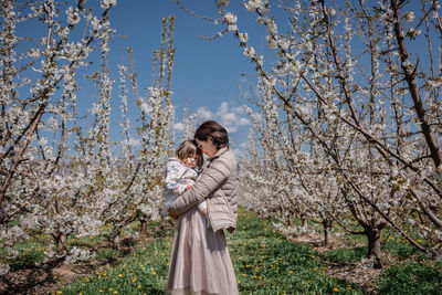 Young woman standing against trees holding her baby