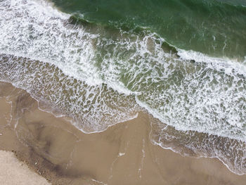 A stunning aerial view of the sea, with waves breaking against a sandy beach.