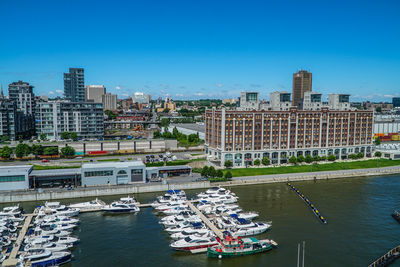 Boats in river by buildings against blue sky