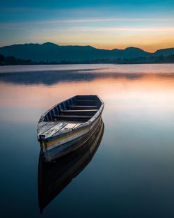 Boat moored on lake against sky during sunset