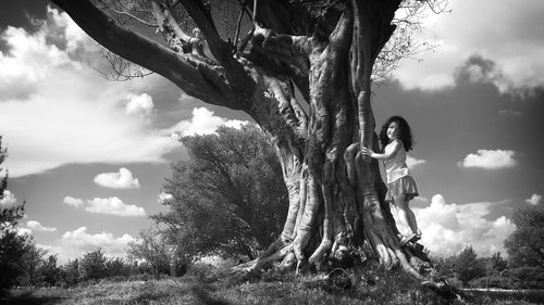 Woman sitting on tree trunk against sky