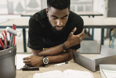 Young male high school student reading book in workshop