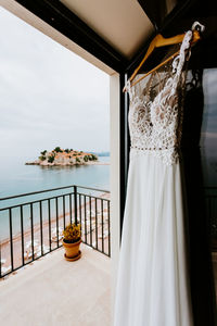 Clothes hanging on railing by sea against sky seen through window