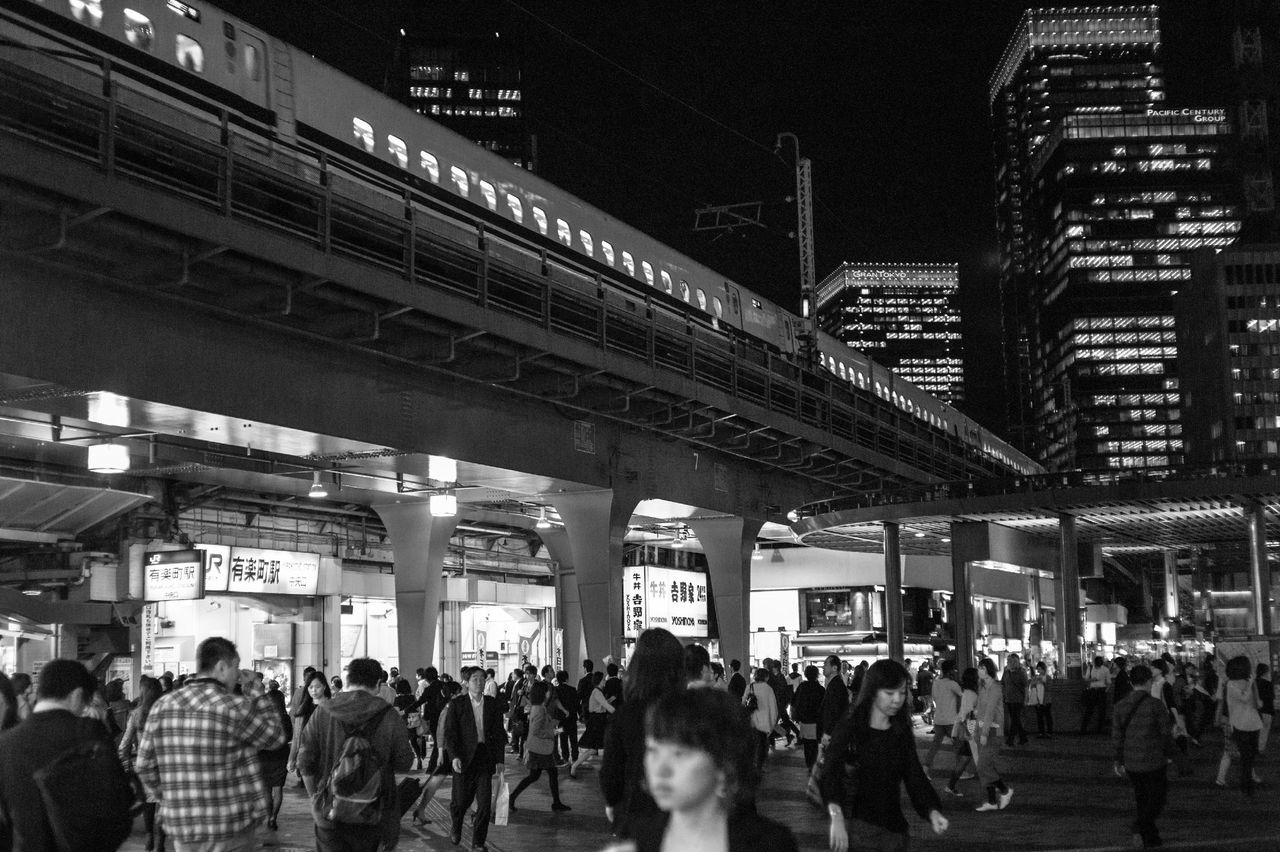 large group of people, architecture, person, built structure, men, lifestyles, building exterior, crowd, city, city life, leisure activity, walking, illuminated, mixed age range, night, text, travel destinations, travel, street