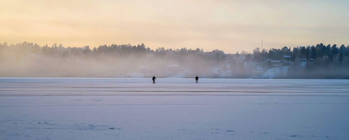 People on snow covered landscape against sky during sunset