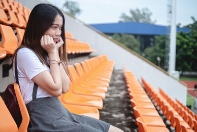 Young woman looking away while sitting on seat at stadium