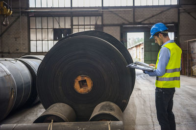 Worker with documents in factory hall with rolls of rubber