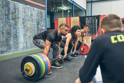 Mixed team lifting weights in the gym with their coach