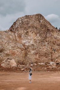 Rear view of woman standing on rock against sky