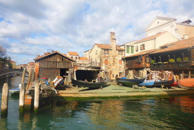 Boats moored in canal by buildings against sky