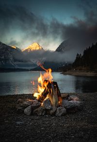 Bonfire at lakeshore against sky during sunset