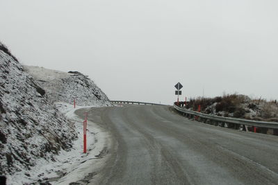 Road leading towards snowcapped mountains against clear sky