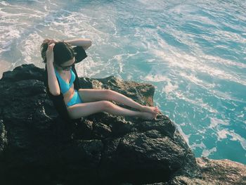 Rear view of woman sitting on rock against sea