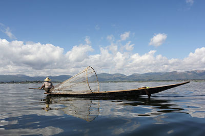 Rear view of fisherman on boat in lake against cloudy sky