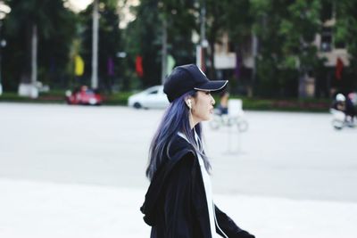 Side view of young woman wearing cap walking in city