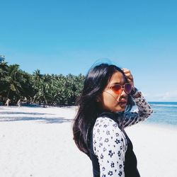 Young woman wearing sunglasses standing at beach against sky