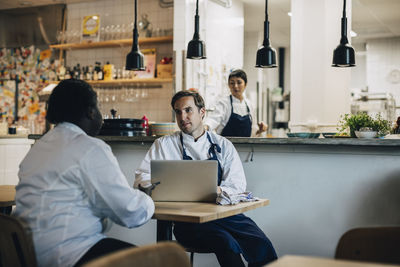 Multiracial chefs discussing business strategy while sitting at table in restaurant