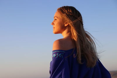 Portrait of woman looking away against clear blue sky