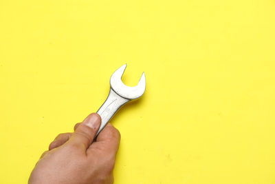 Midsection of person holding hands against yellow wall