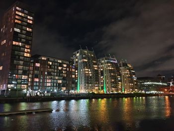 Illuminated buildings by river against sky at night