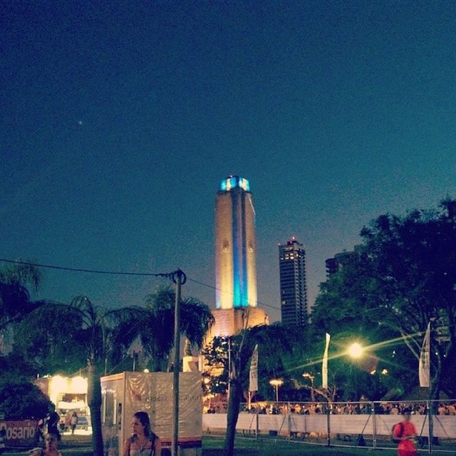 clear sky, building exterior, built structure, architecture, city, illuminated, copy space, blue, street light, transportation, land vehicle, night, sky, tall - high, tree, city life, outdoors, car, men