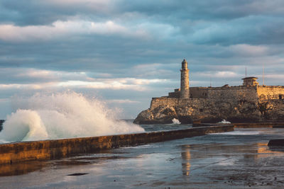 Buildings by sea against cloudy sky