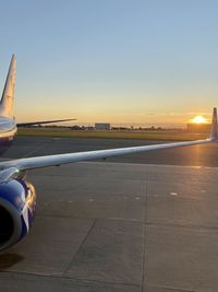 Airplane at airport runway against sky during sunset