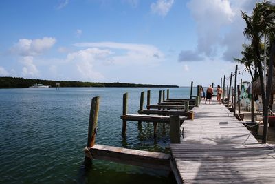 People on pier by sea against cloudy sky