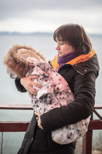 Woman standing in snow with baby on her hands against sky during winter