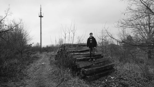 Young man standing on railroad tie at field against sky