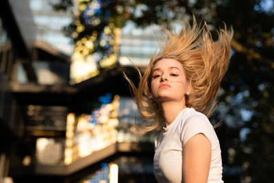 Portrait of young woman standing against tree and buildings