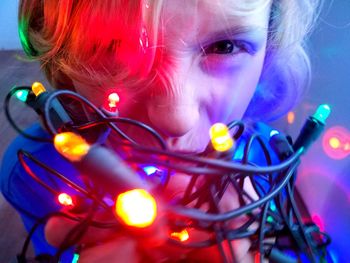 Close-up of boy playing with illuminated string lights at home