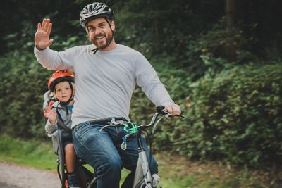 Portrait of father and son waving by cycling against plants