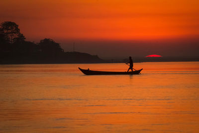 Silhouette man in sea against sky during sunset