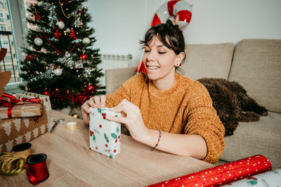 Smiling young woman sitting by christmas tree