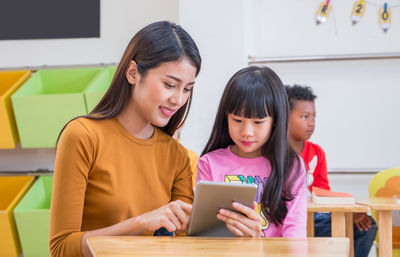 Teacher showing digital tablet to schoolgirl at classroom