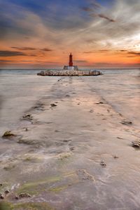 Lighthouse by sea against sky during sunset