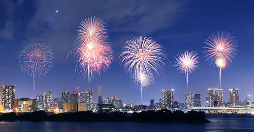 Firework display in city against sky at night