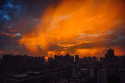 Buildings in city against dramatic sky during sunset