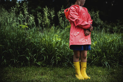 Low section of girl wearing raincoat while standing on grassy field at park during rainy season